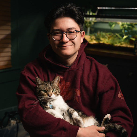 A person holding a cat with a planted aquarium in the background.