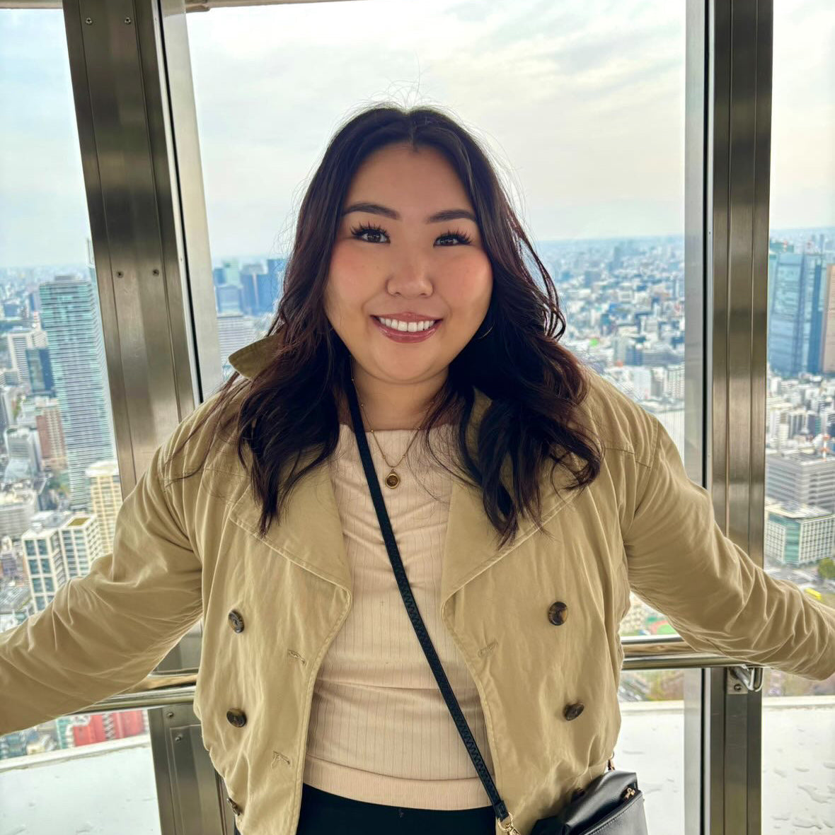 A person with brown hair smiling at the camera with a city skyline in the background.
