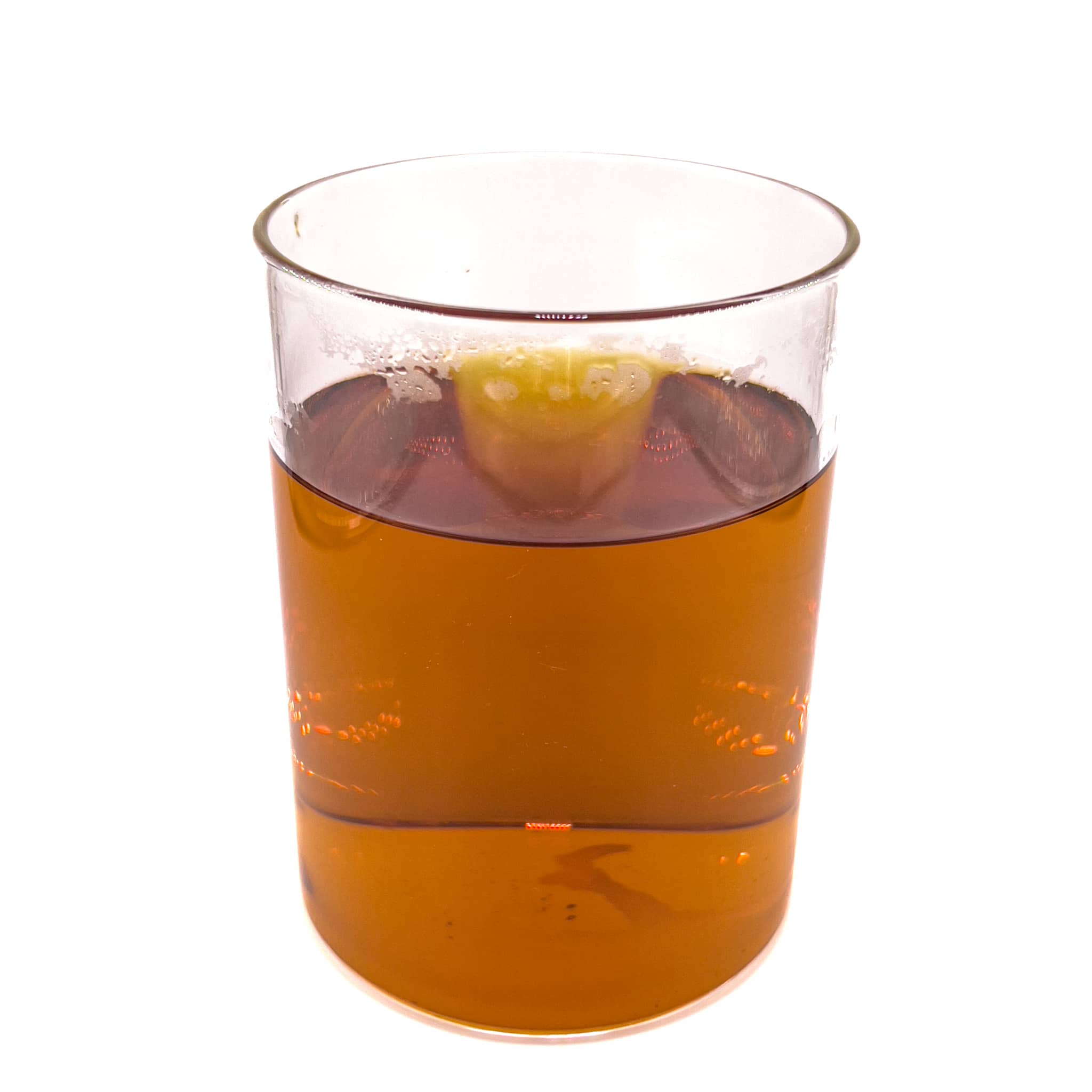 A clear glass jar of aquarium water tinted with amber/yellow tannins from mango leaves by Betta Botanicals.