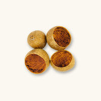 A group of round, golden-brown bael tree pods (Aegle marmelos) with hollow interiors for blackwater aquariums, photographed on a natural background at Betta Botanicals.