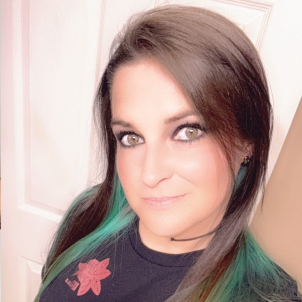 A person with green died hair highlights and a betta botanicals maroon logo on a black tshirt.