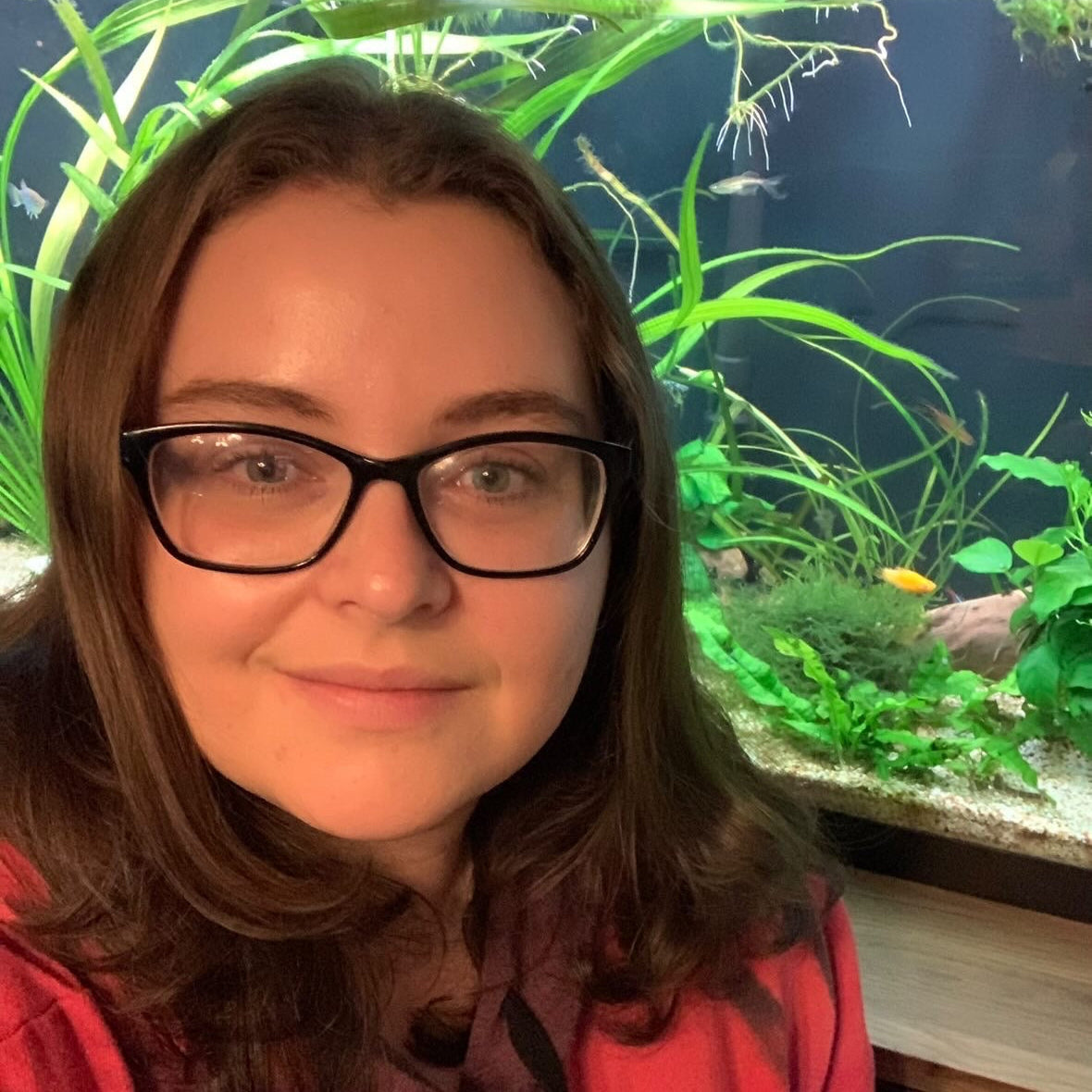 A person wearing black rimmed glasses in front of a planted aquarium.