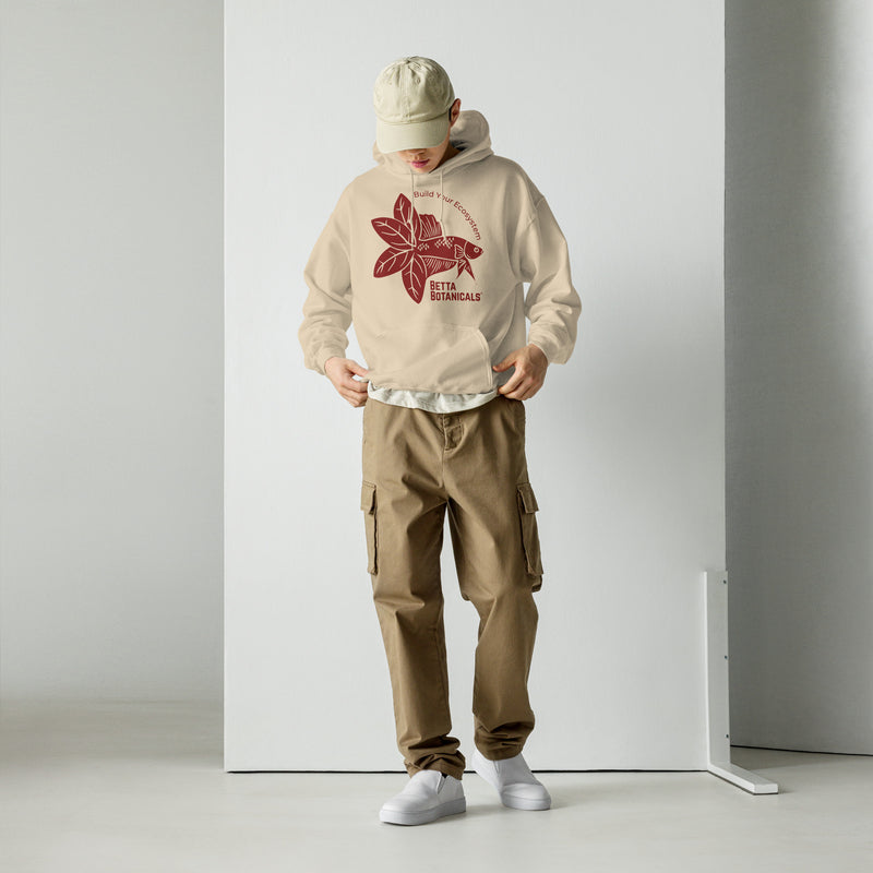 Model dressed in a Betta Botanicals hoodie in sand, displaying a red betta fish and leaf motif paired with ‘Build Your Ecosystem’ text.