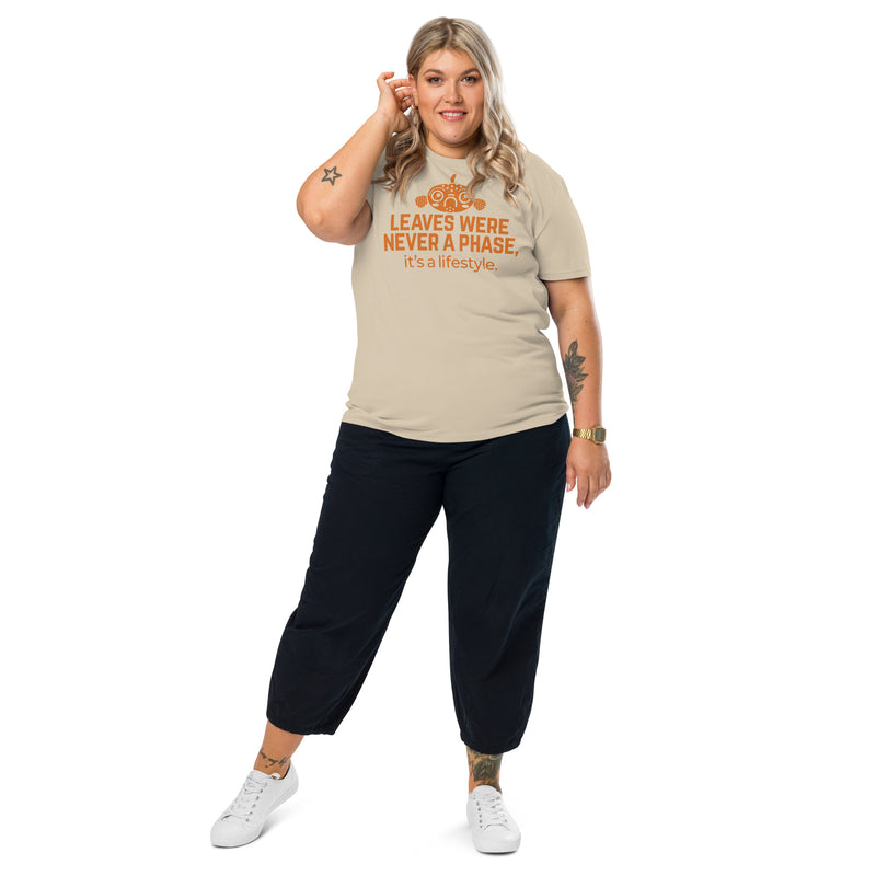 A confident model wearing a beige Betta Botanicals organic cotton t-shirt featuring the slogan ‘Leaves Were Never a Phase, It’s a Lifestyle’ in orange text, paired with black cropped pants and white sneakers, standing against a white background.