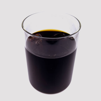 A clear glass jar of aquarium water tinted with dark brown tannins from fermented catappa leaves and Indian almond leaves for by Betta Botanicals.