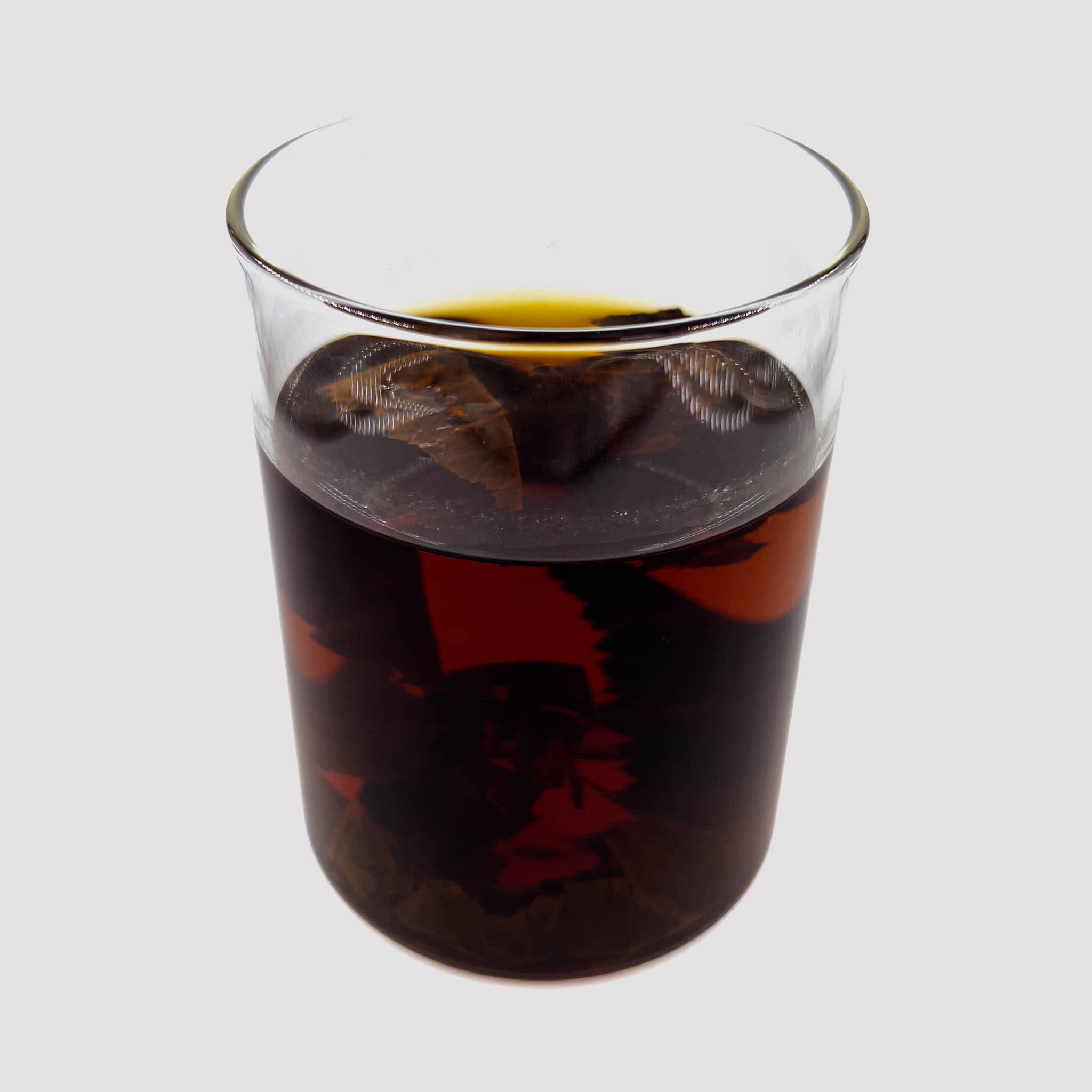 A clear glass jar of aquarium water with brown tannins from small catappa leaves and indian almond leaves by Betta Botanicals.